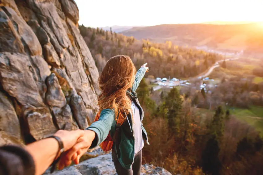 A woman holding her hand out to someone on top of a mountain.