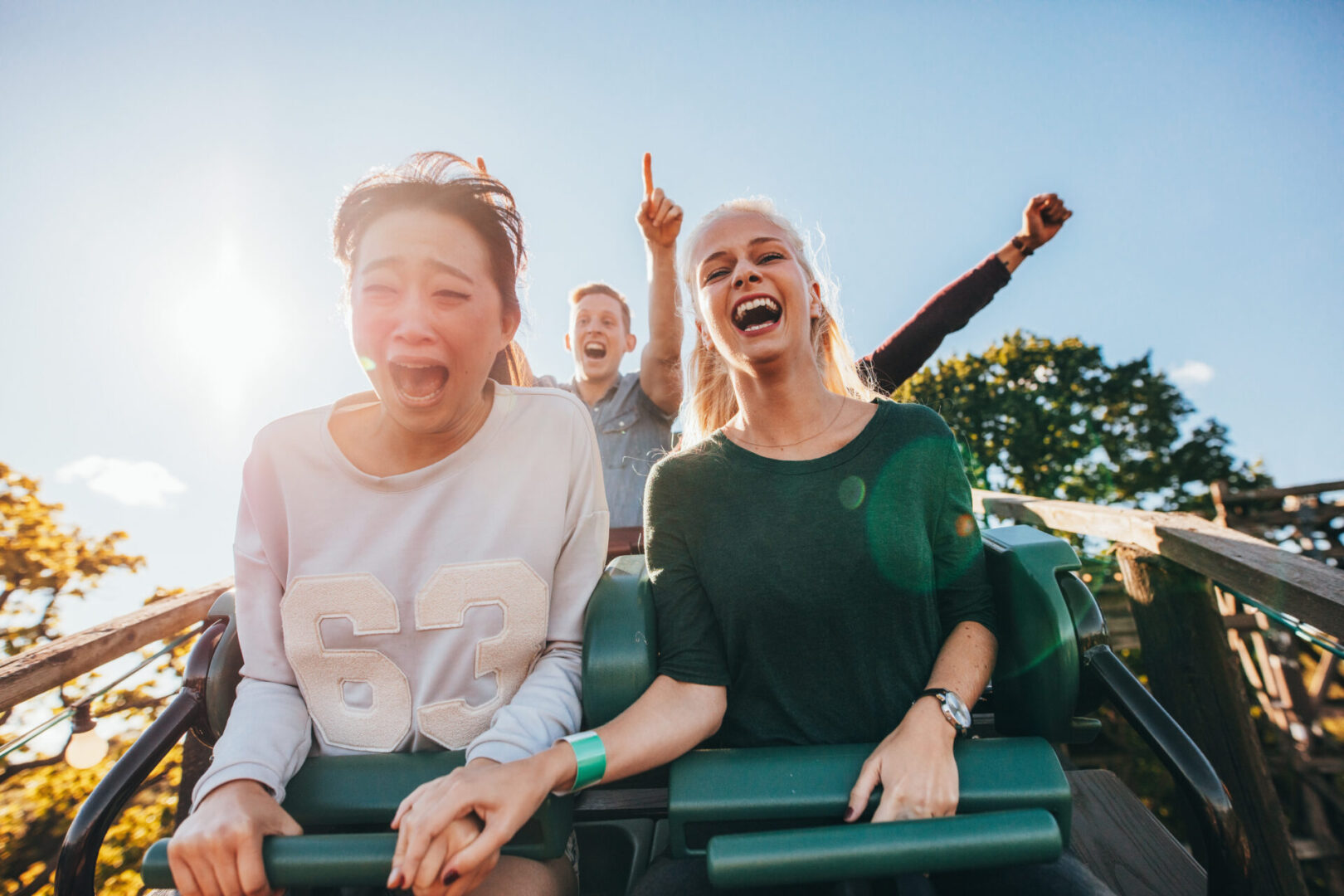 Two women and a man riding on the front of a roller coaster.